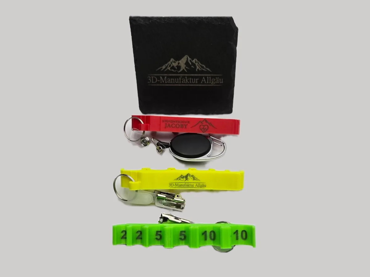 Lasergravierte Halter in Rot, Gelb und Neon Grün vor einer gravierten Schieferplatte