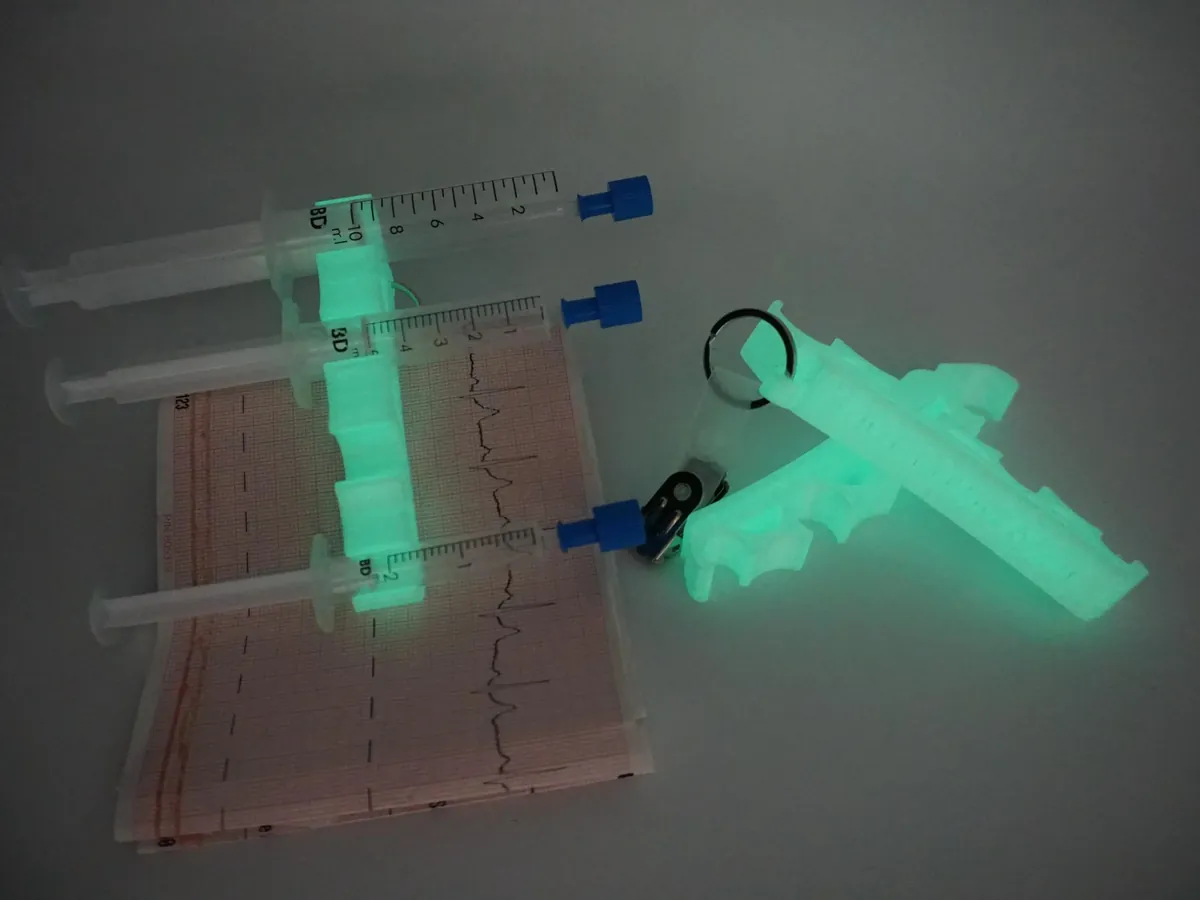 Nachtleuchtender Spritzenhalter 2.0 mit drei Spritzen auf einem EKG-Streifen im Dunkeln