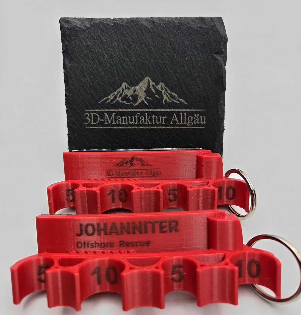 Zwei rote Spritzenhalter vor einer Schieferplatte, vorne die Sonderanfertigung mit Gravur „JOHANNITER Offshore Rescue“