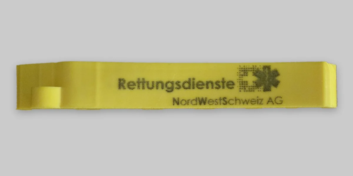 Gelber Spritzenhalter mit Lasergravur „Rettungsdienste NordWestSchweiz AG“ und Logo